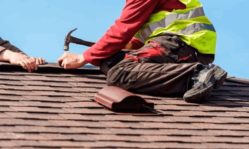 A man sits on the roof and hammers nails